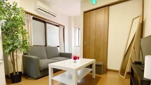 A room with a grey sofa, a white table, a potted plant, and a wooden wardrobe. - SunStay Tachiaikawa II (Tokyo)