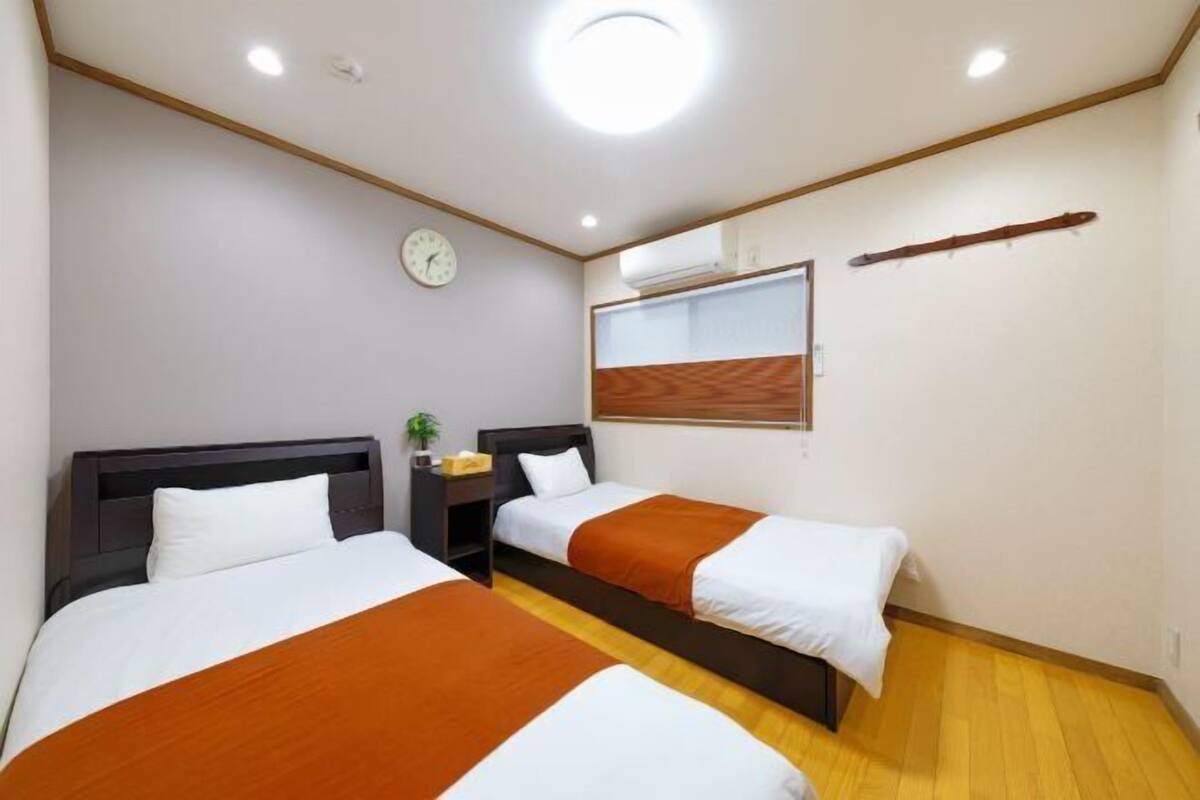 Camera d'albergo con due letti, una sveglia appesa al muro, un condizionatore d'aria e una trave in legno al soffitto.