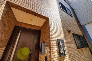 A brick building with a wooden door, a mailbox, and a window with shutters. - AOU･KANZOU (Osaka)