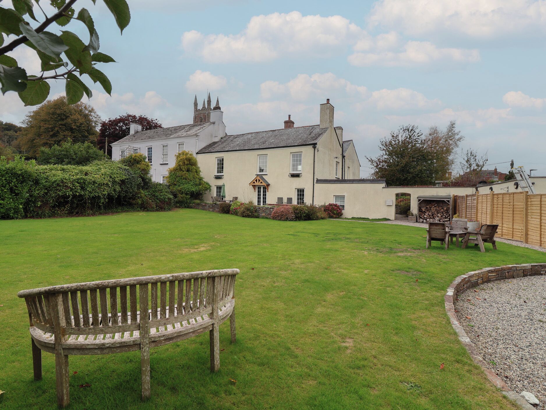 A large, traditional house with a well-maintained lawn, a wooden bench, and a stone wall.