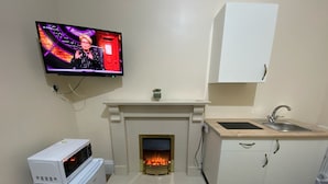 A compact kitchen with a built-in fireplace, a microwave, a sink, and a television mounted on the wall. -  Ground-Floor Super King or Twin Studio Apartment with Free Private Parking (Portsmouth)