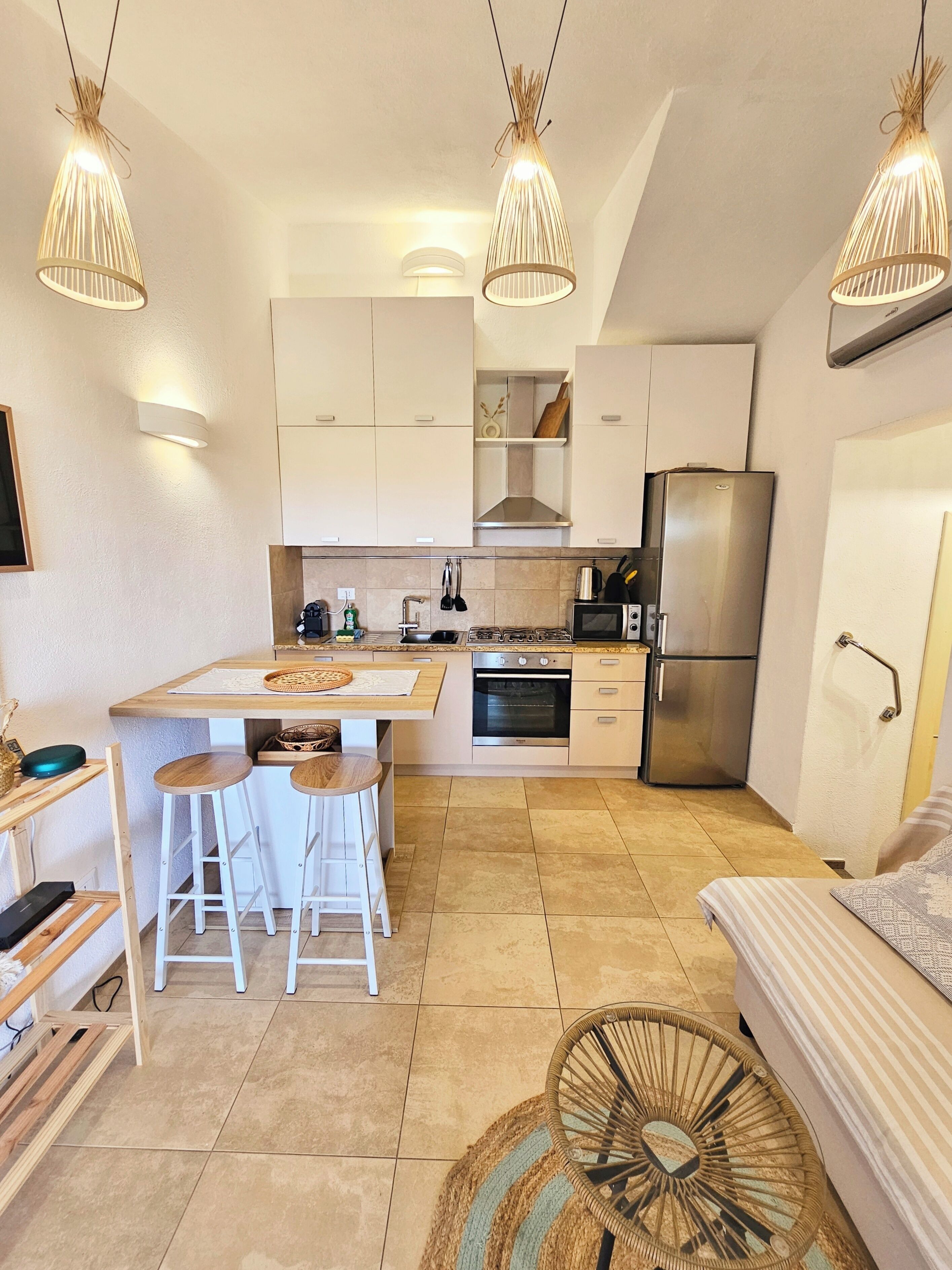 Une cuisine compacte dotée d’appareils électroménagers modernes, un coin repas avec des tabourets et un éclairage suspendu.