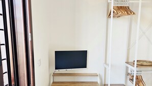 A room with a desk, a chair, a TV, and a shelving unit with clothes. - Charming 2-bedroom house in delightful Baia Sant'Anna with AC (Baia Sant'Anna)