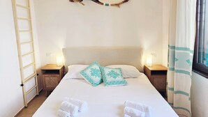 A neatly made bed with white linens, two pillows with a geometric pattern, a wall-mounted branch decoration, and bedside lamps. - Charming 2-bedroom house in delightful Baia Sant'Anna with AC (Baia Sant'Anna)