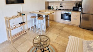 A modern kitchen with white cabinets, a stainless steel refrigerator, a built-in oven, and a microwave. There are two bar stools and a round woven rug on the floor. - Charming 2-bedroom house in delightful Baia Sant'Anna with AC (Baia Sant'Anna)