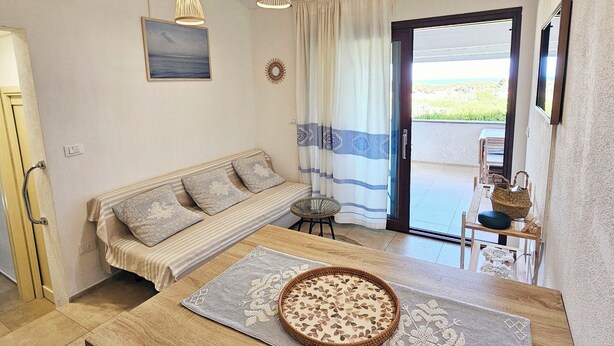 A modern kitchen with a wooden island, pendant lights, a sofa, and a view through a glass door. - Charming 2-bedroom house in delightful Baia Sant'Anna with AC (Baia Sant'Anna)