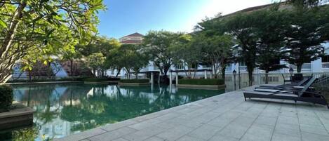 A tranquil outdoor pool area with a tiled deck, surrounded by trees and a white fence.