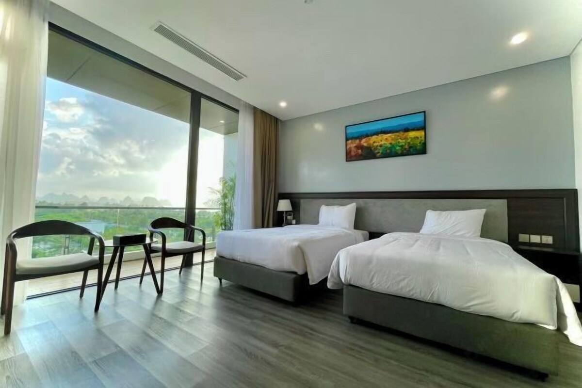 A modern hotel room with two beds, a balcony with a view, and a painting on the wall.
