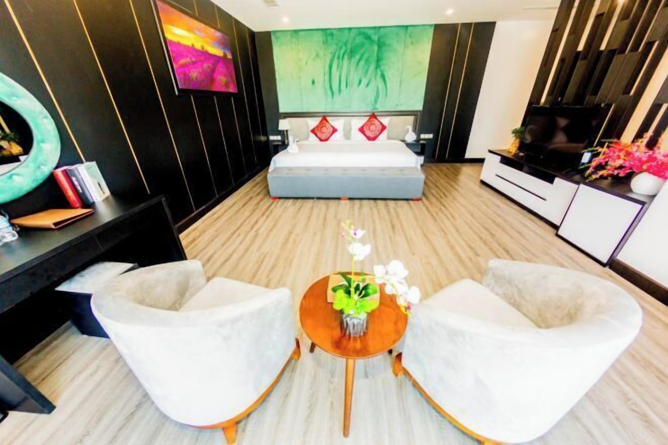 A modern bedroom with a large bed, a TV, and a seating area with two chairs and a small table.