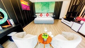 Een moderne slaapkamer met een groot bed, een televisie en een zithoek met twee stoelen en een tafeltje.