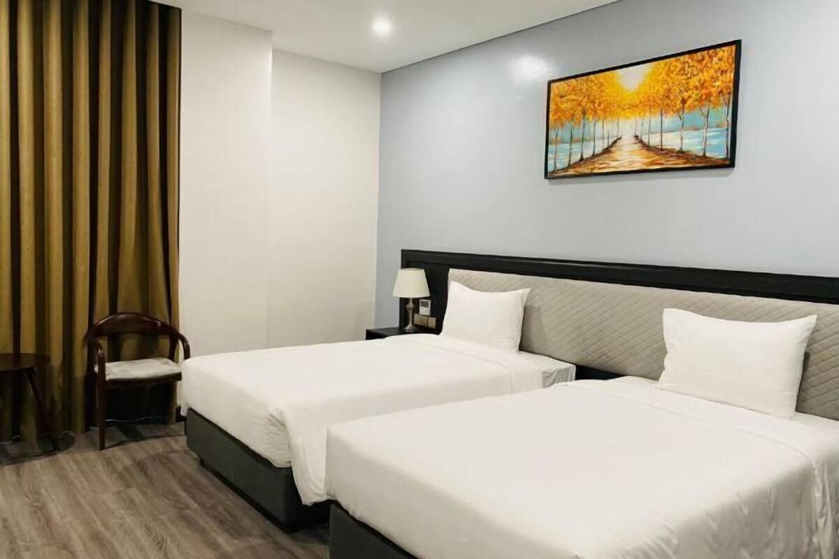 A hotel room with two beds, a wooden chair, a nightstand with a lamp, and a painting on the wall.