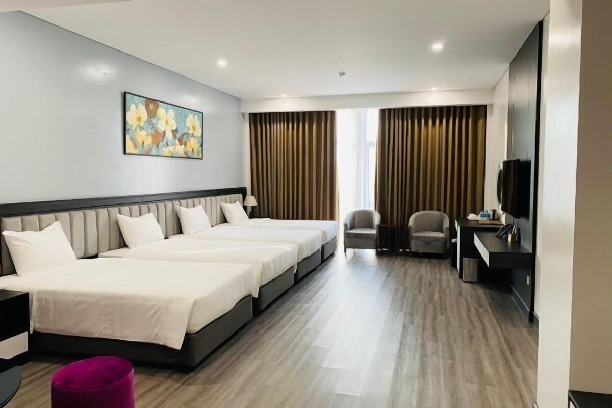 A hotel room with three beds, a desk, a chair, and a television.