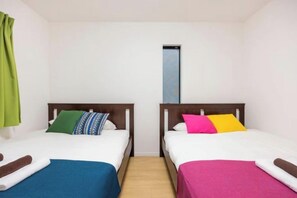 Una stanza con due letti, ognuno con una coperta e dei cuscini di colore diverso.