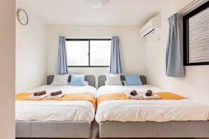 A hotel room with two beds, a window with curtains, an air conditioning unit, and a clock on the wall. - Higashi Mukoujima 6 chome (Tokyo)