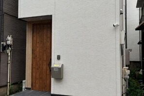 A building entrance with a wooden door, a mailbox, and a security camera. - Higashi Mukoujima 6 chome (Tokyo)