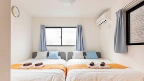 A hotel room with two beds, a window with curtains, an air conditioning unit, and a clock on the wall. - Higashi Mukoujima 6 chome (Tokyo)