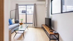 A modern living room with a sofa, a glass coffee table, a TV on a wooden stand, and a large window with curtains. - Higashi Mukoujima 6 chome (Tokyo)