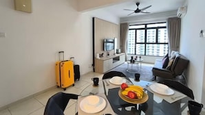 A hotel room with a dining table, chairs, a yellow suitcase, a TV, and a sofa. - The Garden Homestay BySTAY (Sekudai)