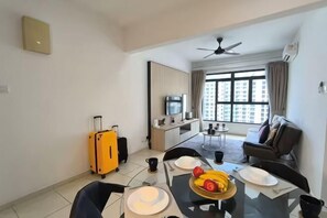 Une chambre d’hôtel avec une table à manger, des chaises, une valise jaune, un téléviseur et un canapé.
