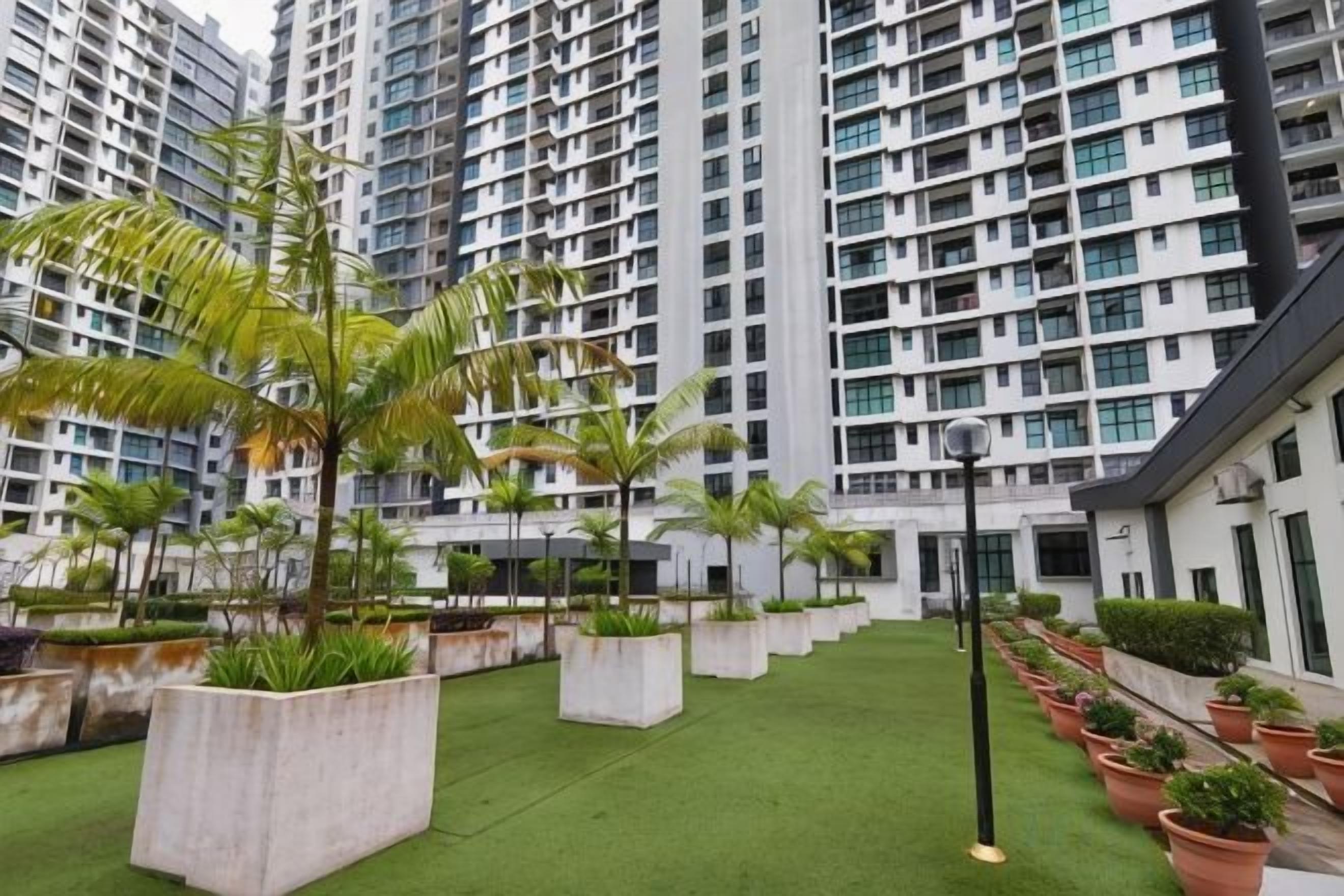 A courtyard with artificial grass, potted plants, and tall residential buildings in the background.