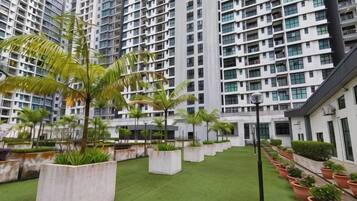 A courtyard with artificial grass, potted plants, and tall residential buildings in the background.