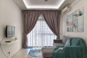 A living room with a TV, a sofa, a window with curtains, and artwork on the wall. - The Garden Homestay BySTAY (Sekudai)