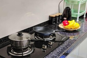 Een keuken met een fornuis, een koekenpan, een pan en een schaal fruit.