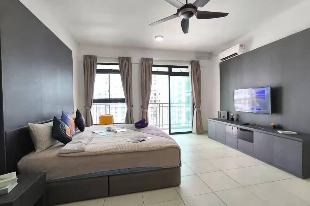 Une chambre d’hôtel moderne dotée d’un grand lit, d’une télévision, d’un ventilateur de plafond et d’un balcon avec des rideaux.