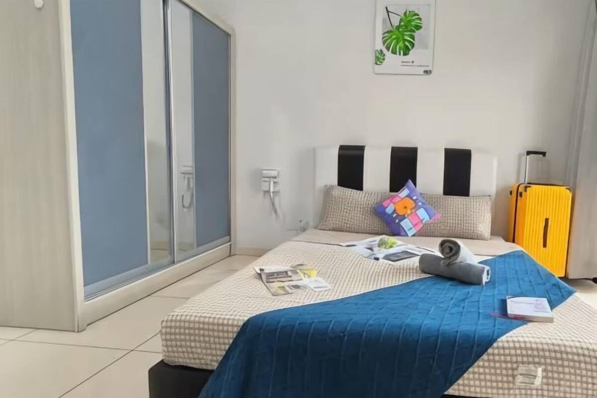 Une chambre d’hôtel avec un lit, une valise, une plante et une porte coulissante.