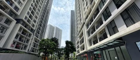 Una calle urbana moderna con edificios altos, cielo despejado y una zona arbolada central.