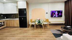 A modern living room with a dining area, a kitchen, and a TV. - 2BRS@Vinhomes Smart City (Hanoi)