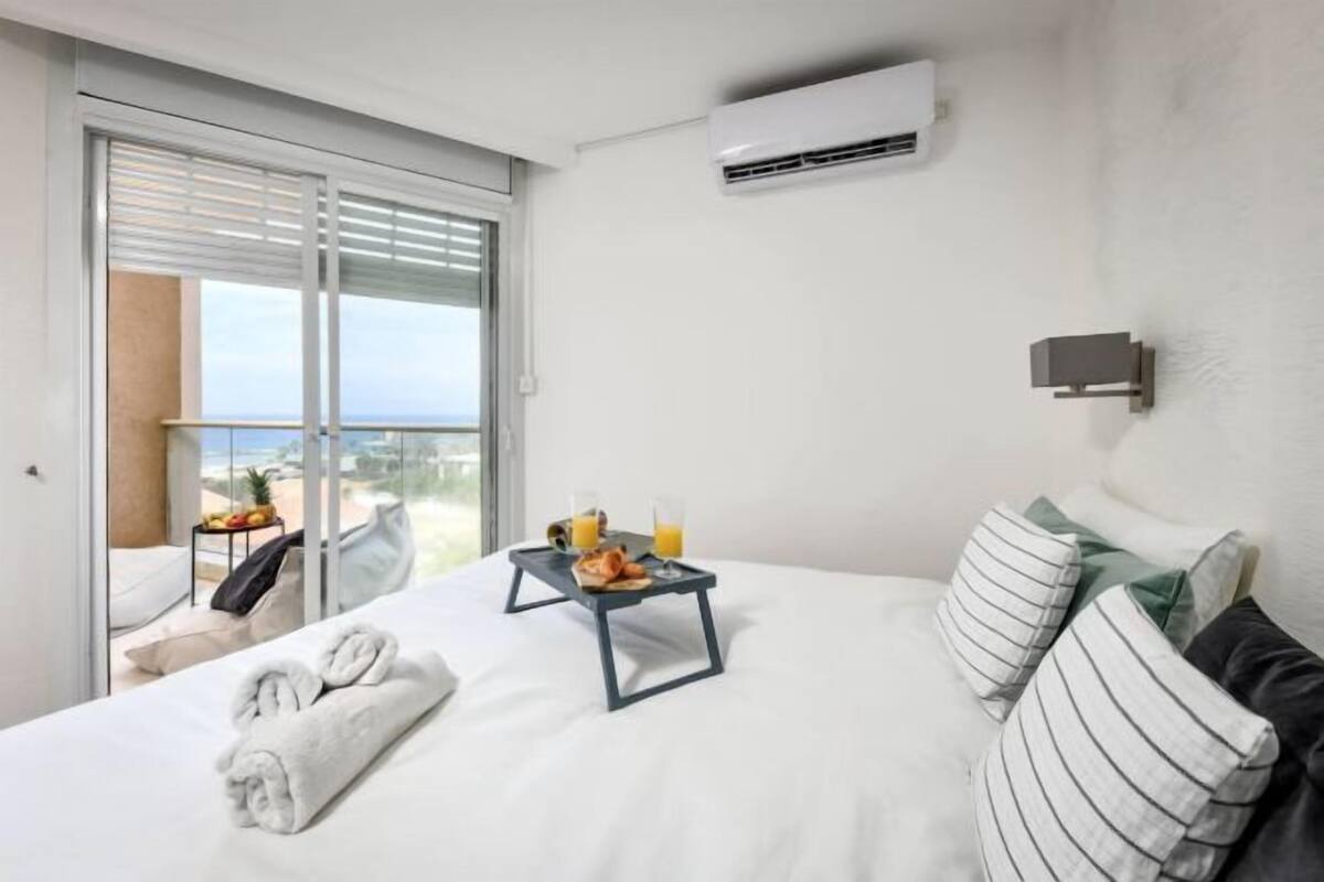 Habitación de hotel con una cama, una bandeja con alimentos para el desayuno, una toalla y vistas al exterior a través de una puerta corrediza.
