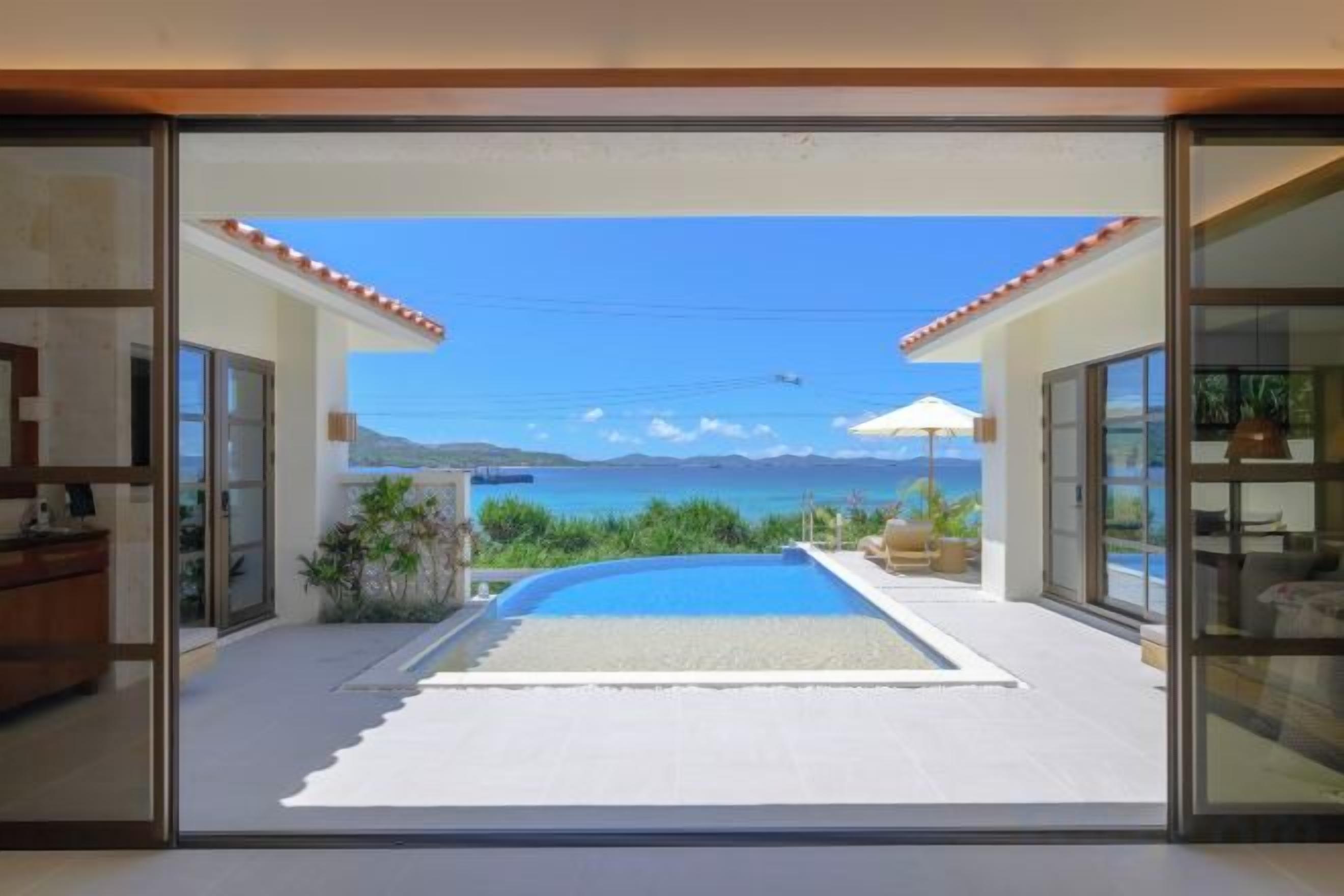 A modern house with a glass door leading to a pool and a view of the sea.
