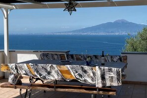 A terrace with a table and chairs, overlooking a coastal view with a mountain in the distance. - Villa L'Ulivina - Indipendent Villa Garden & View (Sorrento)