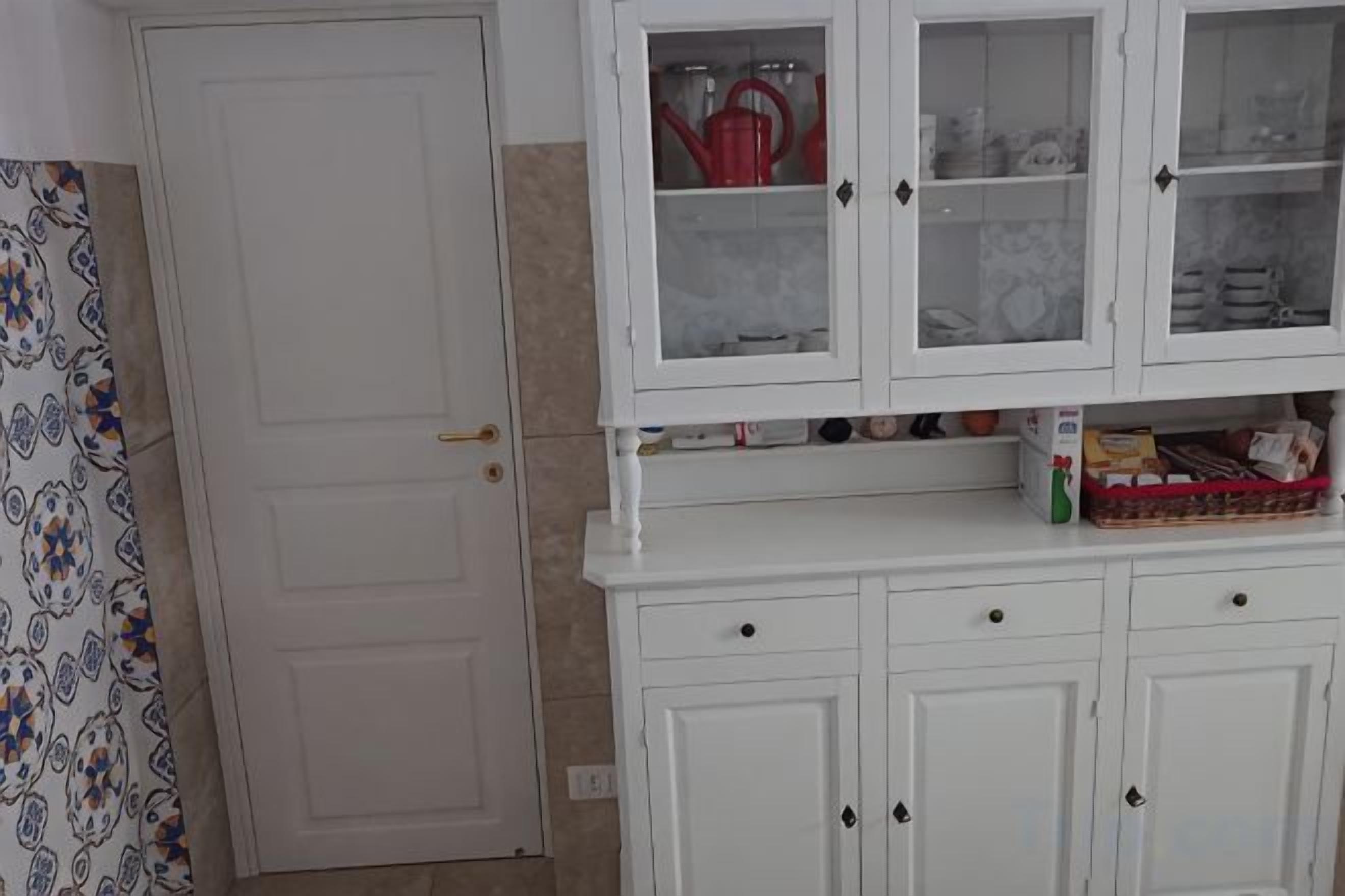 Una cocina con armarios blancos, una puerta y una cortina estampada.