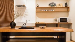 A kitchen with a wooden table, a microwave, and shelves with decorative items. - KIRAKU・SATOZAKURA (Kyoto)