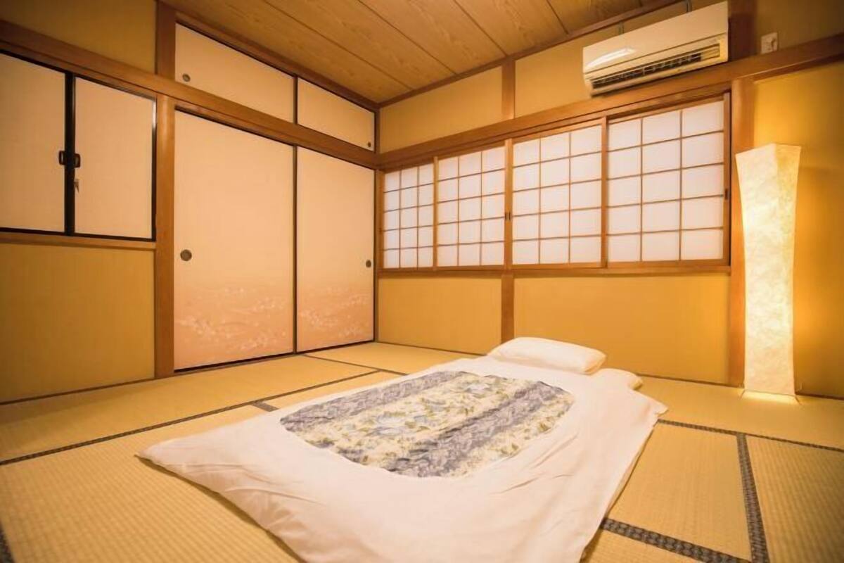 A traditional Japanese room with tatami flooring, a futon bed, sliding doors, and a large window with a view.