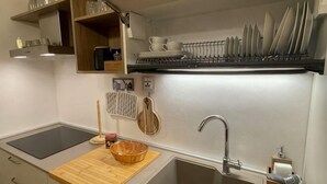 A compact kitchen with a sink, a wooden cutting board, a basket, and a dish rack above the sink. - The Crystal Suite - Gorizia Central Apartment (Gorizia)