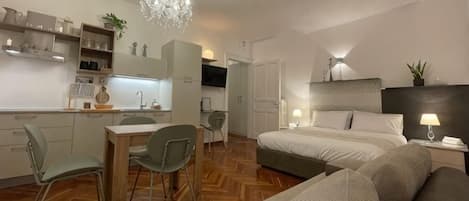 Una habitación de hotel compacta con kitchenette, comedor, cama y zona de estar.