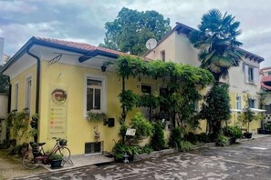 A yellow building with a red roof, potted plants, and a bicycle. - The Crystal Suite - Gorizia Central Apartment (Gorizia)