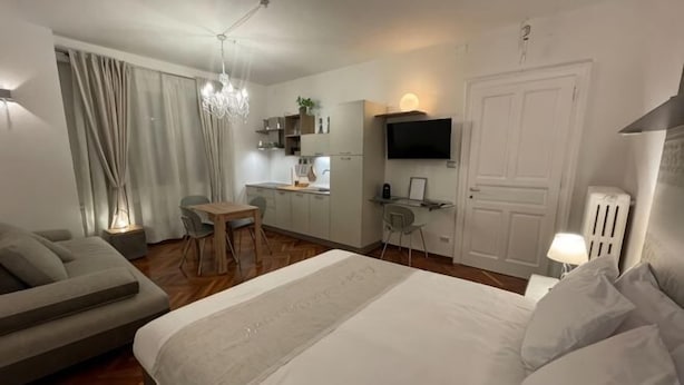 A modern hotel room with a bed, a sofa, a dining table, a TV, and a kitchenette. - The Crystal Suite - Gorizia Central Apartment (Gorizia)