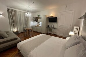 A modern hotel room with a bed, a sofa, a dining table, a TV, and a kitchenette. - The Crystal Suite - Gorizia Central Apartment (Gorizia)