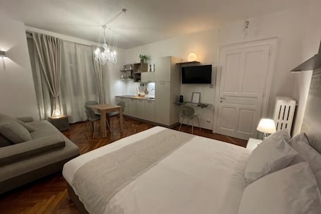A modern hotel room with a bed, a sofa, a dining table, a TV, and a kitchenette.. The Crystal Suite - Gorizia Central Apartment