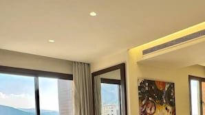 Camera d'albergo con un letto grande, una scrivania, una sedia, un quadro e vista sul mare.