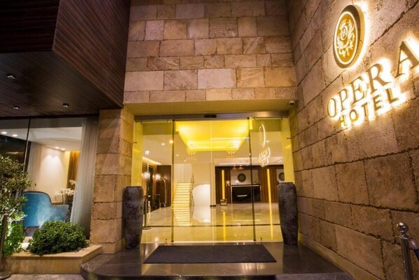 The entrance of the Opera Hotel with a stone facade and a sign above the door.