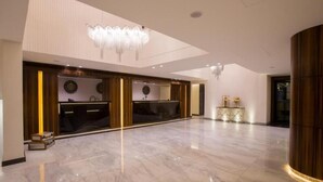 Un'ampia hall con pavimento in marmo, una reception, un lampadario e una parete decorativa con un orologio.