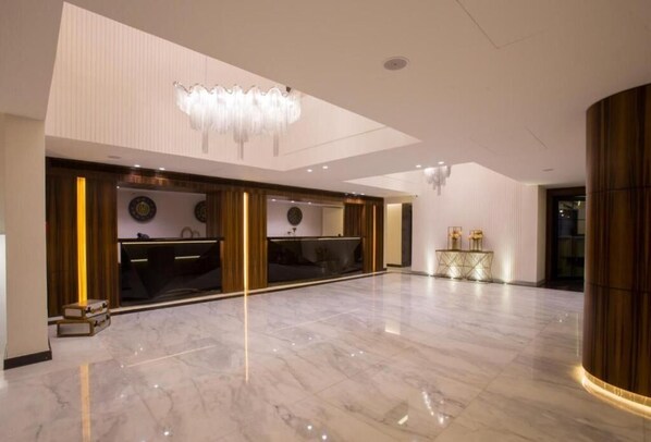 A spacious lobby with a marble floor, a reception desk, a chandelier, and a decorative wall with a clock. - OPERA HOTEL  (Kfar Yassine)