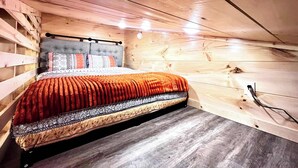 Ein Schlafzimmer mit Holzboden und geneigten Wänden, einem Bett mit gemusterten Bettwaren sowie einer sichtbaren Steckdose.