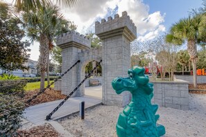 Un parque con una estructura que parece castillo, una estatua de dragón verde y columpios.