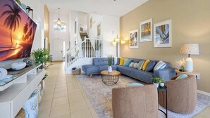 Ein geräumiges Wohnzimmer mit großem Fernseher, einer Treppe und einer gemütlichen Sitzecke.